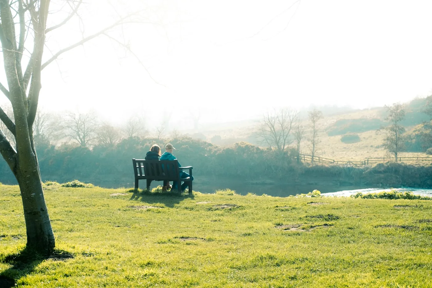 A retired couple sitting together on a bench, looking out over misty countryside
