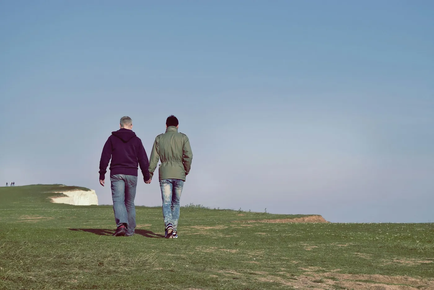 Two people walking together across a clifftop meadow, hand in hand