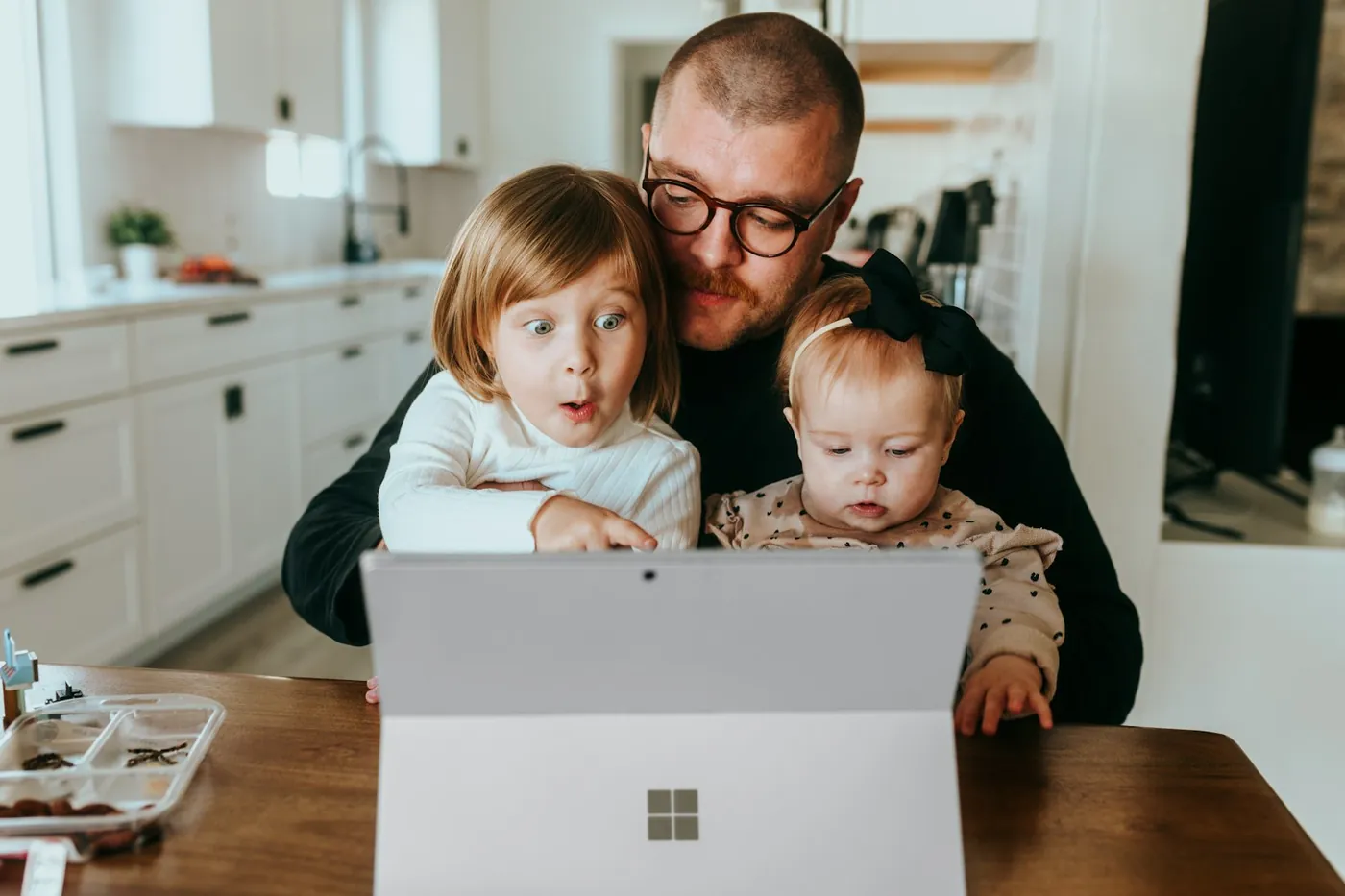 A dad at the kitchen table with his two young children, all looking at one screen together